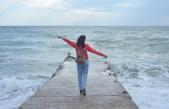 Rear view of a young woman tourist with a backpack standing on the pier and waves hitting the pier in a storm. City of Sudak, Crimea. photo