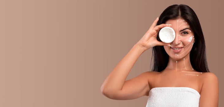 A woman enjoys her skin care routine while holding a jar, ready to apply a treatment. She is isolated against a neutral background, creating a calm and focused atmosphere for her beauty ritual. photo