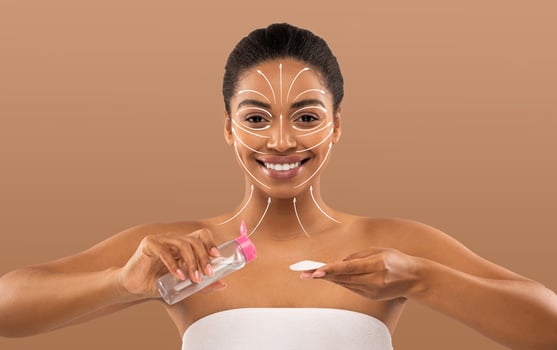 African American woman engaged in her beauty routine smiling confidently while applying skincare. The neutral background emphasizes her focus on self-care and pampering. photo