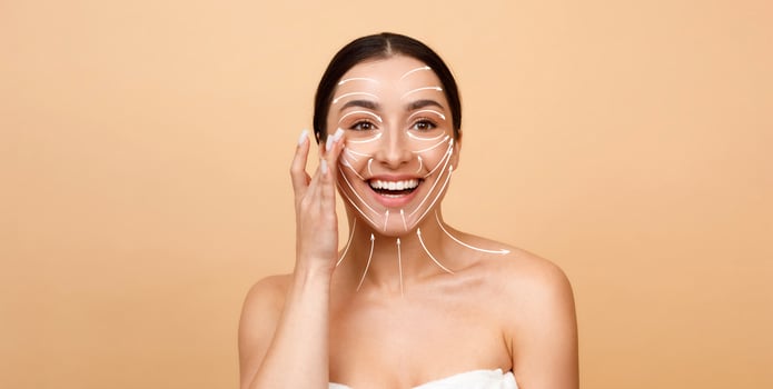 A woman with a radiant smile applies skincare products on her face, showcasing a glow. The setting features an isolated background, emphasizing her beauty and self-care moment. photo