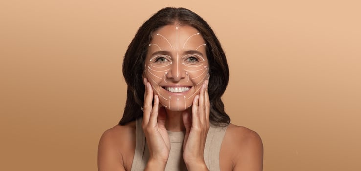 A woman is enjoying her skin care routine, smiling while applying products to her face. The softly lit background enhances the focus on her radiant skin and joyful expression, perfect for relaxation. photo