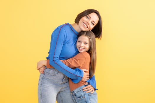 A mother and daughter embrace each other with smiles against a bright yellow background. Their joyful connection highlights the affection and strong bond they share in this tender moment. photo