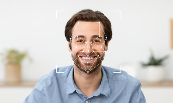 A young man is smiling while facial recognition technology analyzes his features. He is seated in a relaxed environment with greenery visible in the background, indicating a calm atmosphere. photo