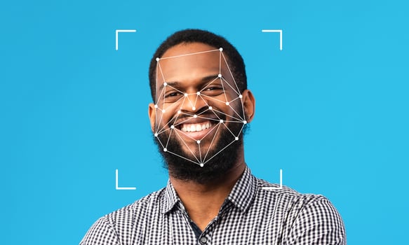 A man smiles confidently against a blue background as facial recognition technology analyzes his features. This highlights advancements in identification processes and their growing presence. photo