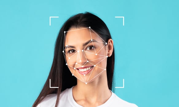 A young woman with long dark hair smiles brightly, her face framed by a blue background. Facial recognition technology highlights her features, emphasizing identification capabilities. photo