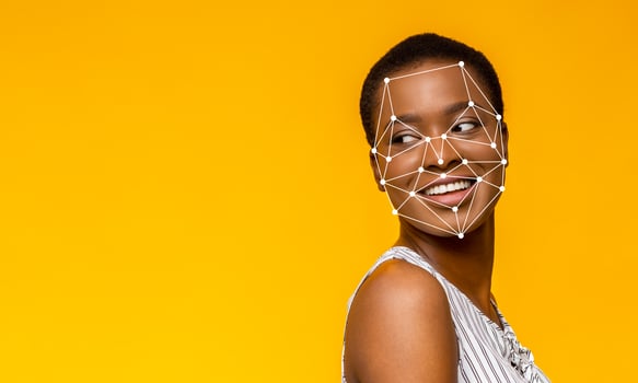 A young woman with a joyful expression turns her head slightly to the side against a vibrant yellow backdrop. Facial recognition points are superimposed on her face, illustrating modern technology. photo