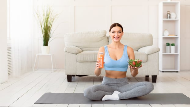 Fit Woman Holding Salad And Fruit Juice Sitting On Gymnastic Mat Slimming At Home. Healthy Diet Concept. Panorama photo