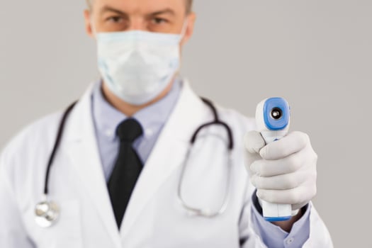 Closeup portrait of doctor wearing protective surgical mask ready to use infrared forehead thermometer gun photo