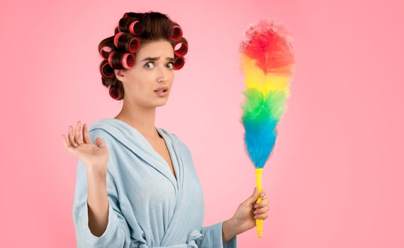 Spring Cleaning. Confused Glamorous Lady With Hair Curlers Holding Feather Duster Doing House Chores Looking At Camera In Shock Standing Over Yellow Studio Background. Housework Concept photo