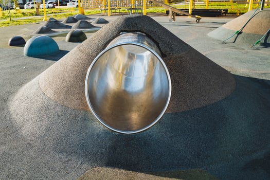 A metal pipe is going down a hill in a playground photo