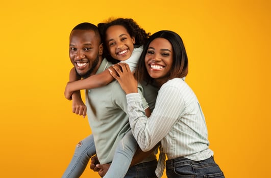Time with family. Overjoyed african american family laughing and posing to camera isolated over yellow studio wall. Cheerful father carrying his daughter on back photo