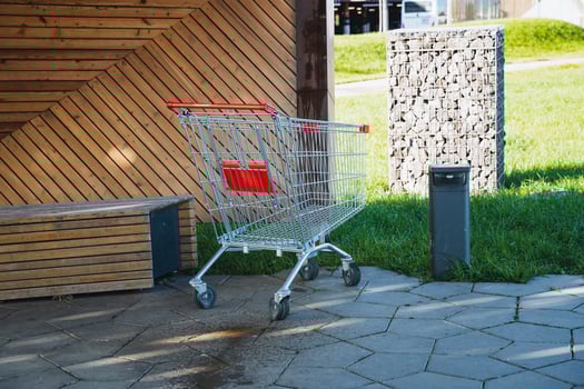 An empty shopping cart is currently parked on the sidewalk right in front of a wooden bench, creating a scene that captures the essence of everyday life in an urban environment photo