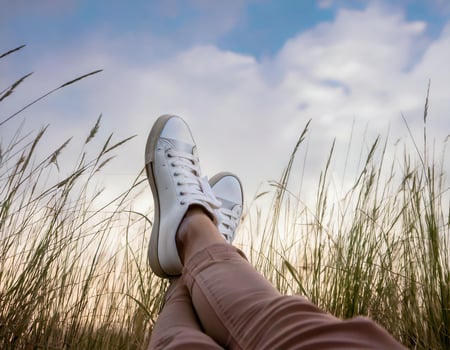 Raised feet with white shoes on the meadow with blue sky background photo