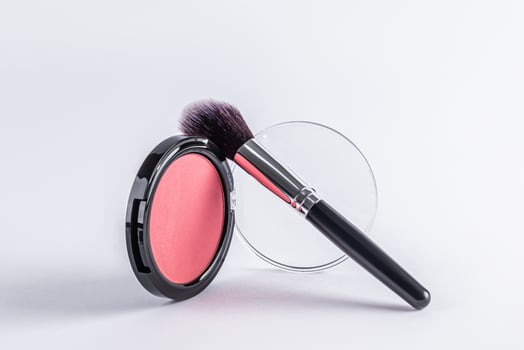 Front view of a beautiful open round pack of pink blush with a professional black makeup brush on it. white background. Product layout. A copy space. photo