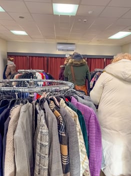 Thrift store shoppers browse racks of clothing. High quality photo