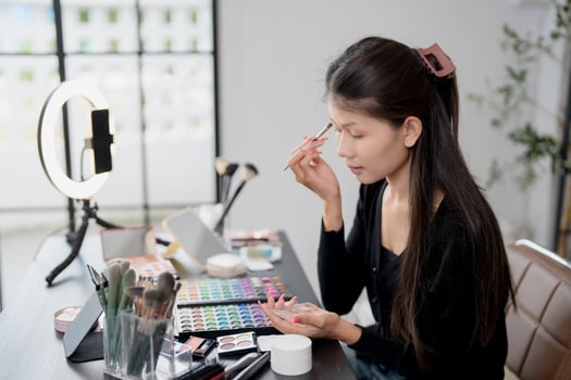 a beauty influencer woman is applying makeup in front of a mirror photo