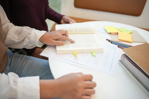 two people sitting at a table with books and pens learning together photo