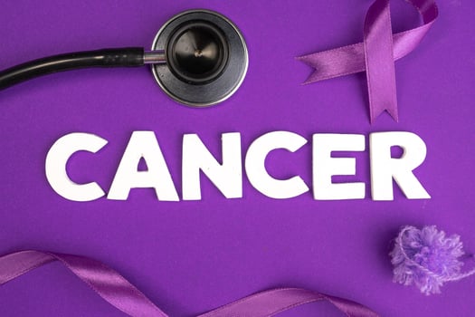 A stethoscope purple ribbons and the word CANCER are arranged on a purple background. Cancer awareness concept background photo