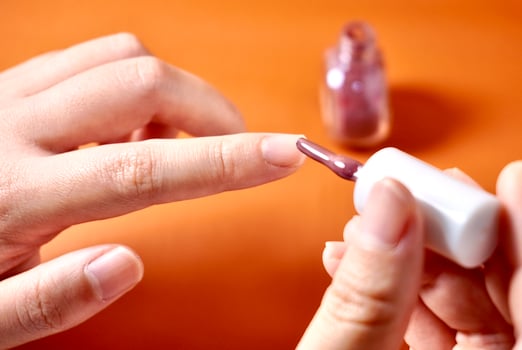 Hand applying nail polish on fingernail isolated on horizontal orange brown terracotta colored background. photo