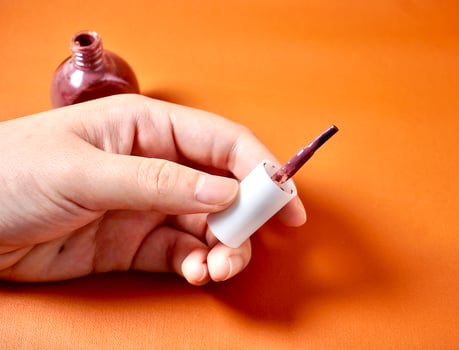 Hand holding nail polish brush isolated on horizontal orange brown terracotta colored background. photo