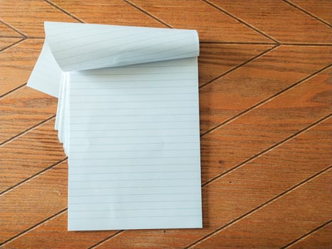 Blank lined notepad pages partially rolled, resting on a brown woodgrain surface. Perfect for showcasing your message, quotes, or product information. photo
