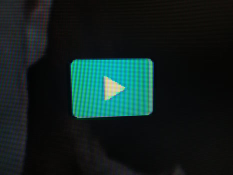 Closeup shot of a vibrant teal play button on a dark screen, showcasing the pixelated texture. Ideal for technology, media, and entertainment projects needing a modern and sleek visual. photo