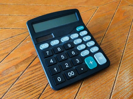A slightly dusty, black calculator rests on a warm brown wood surface. Its simple design and clear display make it perfect for illustrating concepts of finance, math, or everyday calculations. photo