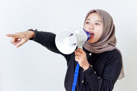 A woman passionately speaks through a megaphone while pointing forward. photo