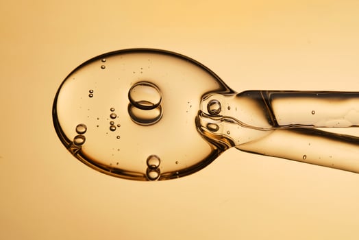 A beautiful drop of gel-like cosmetic serum with bubbles on a golden background. photo