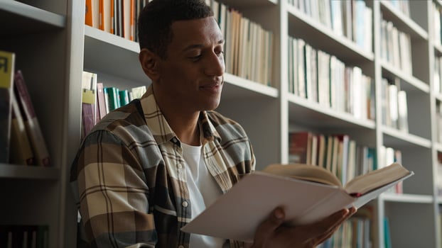 African American man sitting library floor bookcase reading book pleasure hobbies story knowledge learning student turning pages male guy academy study literary university history interesting reader photo