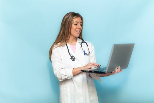 Smiling doctor woman working with laptop on blue background photo