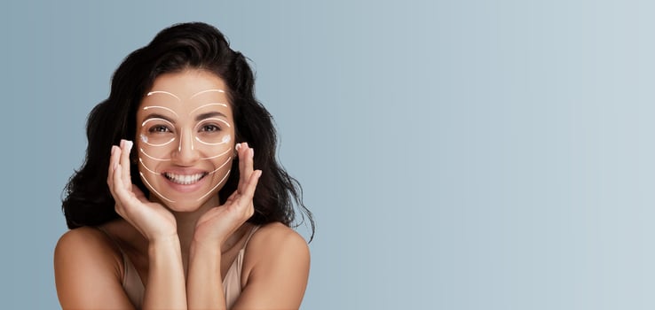 A woman engages in her beauty routine, applying skincare products to enhance her natural glow. She smiles confidently, surrounded by a serene, light-filled space perfect for pampering. photo
