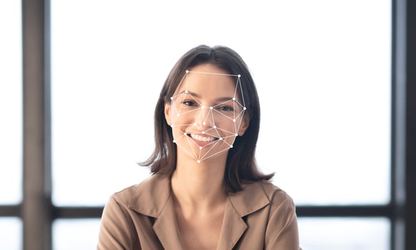 A woman with a cheerful expression sits in a well-lit environment as facial recognition technology analyzes her features. The background is plain, emphasizing her face. photo