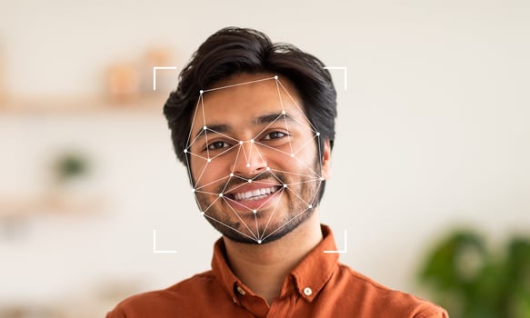 A young man with a cheerful expression stands in a well-lit indoor environment. Facial recognition technology highlights his face, indicating advancements in identification and security. photo