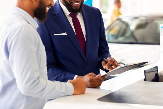 Joyful Black Man Buying Car, Signing Papers With Salesman In Dealership Office, Happy Young African American Male Consulting With Manager While Purchasing New Vehicle In Modern Showroom, Copy Space photo