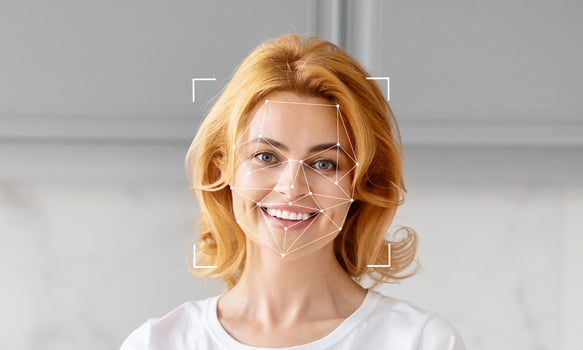 A person with blonde hair smiles while standing in a contemporary indoor environment. Their face is highlighted by facial recognition technology for identification purposes, emphasizing innovation. photo
