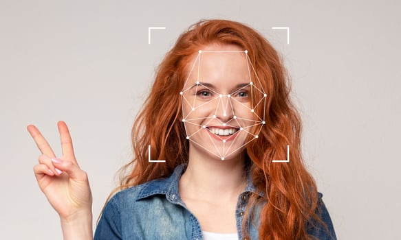 A young woman with vibrant red hair smiles widely while making a peace sign with her hand. Facial recognition markers are displayed on her face, highlighting the technology in action. photo