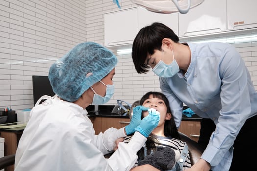 Asian female pediatric dentist examines girl's teeth in dental clinic and takes care and encourages of father, mouth oral hygiene, and professional orthodontic healthcare work in a kid hospital. photo