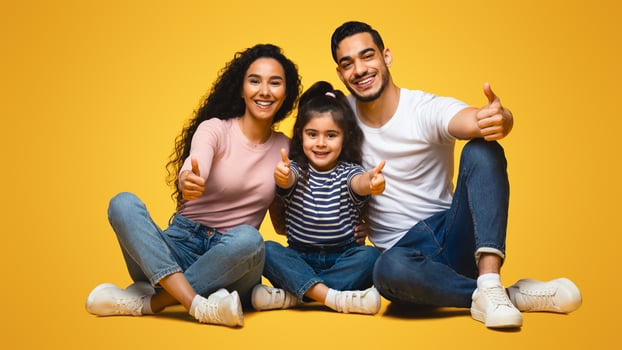 Like Concept. Happy Middle Eastern Family Of Three Showing Thumbs Up At Camera While Sitting Over Yellow Studio Background, Happy Arab Parents And Little Daughter Approving Or Recommending Something photo