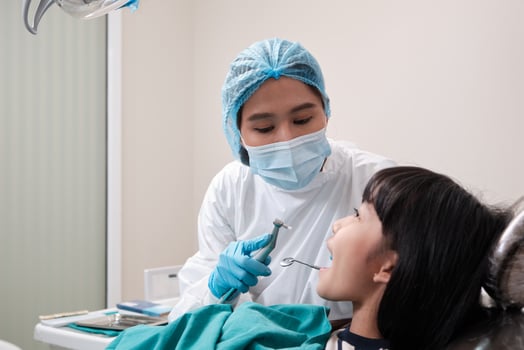 Asian female pediatric dentist checks and examines a little girl's caries teeth in dental clinic, well-being mouth oral hygiene, and professional orthodontic healthcare work in a kid hospital. photo