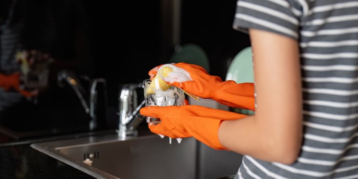 Close up of a young woman washing a soapy glass at the kitchen sink, wearing orange gloves photo