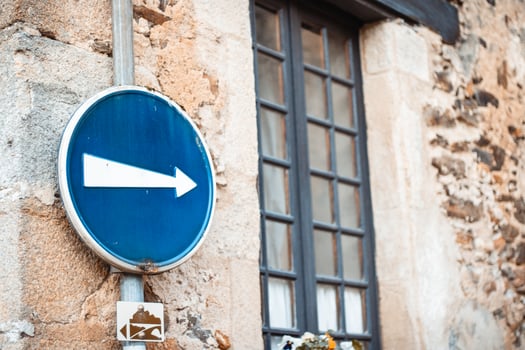 Blue and white arrow direction traffic sign against the house wall photo