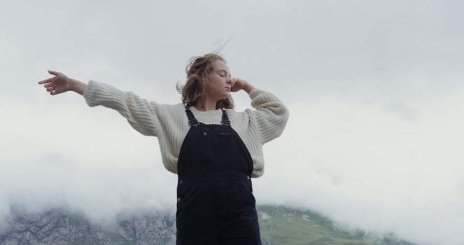 Russia, Caucasus. A beautiful young woman of European appearance, dressed in a warm sweater, stands on the parapet against the background of green hills and makes smooth movements with her hands photo