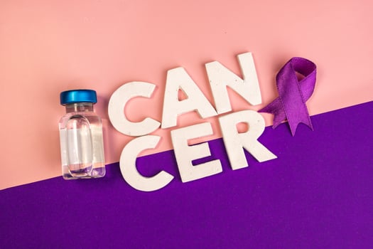 A vial sits next to the word CANCER and a purple ribbon. International cancer day concept background photo