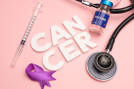 A vaccine syringe stethoscope and purple ribbon lie near the word CANCER. World cancer day concept background photo