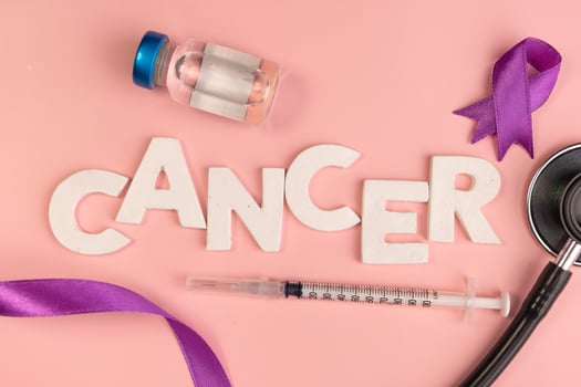 The word CANCER is spelled out in white letters next to a vial syringe stethoscope and purple ribbons photo