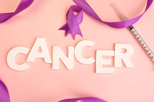 The word CANCER is spelled out in white letters accompanied by purple ribbons and a syringe photo