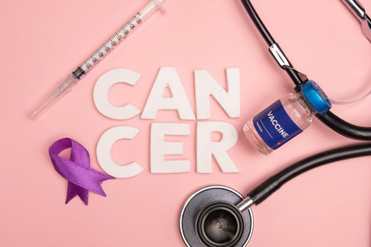 A vaccine vial and medical tools lay near the word cancer and a purple ribbon. World cancer day concept background photo