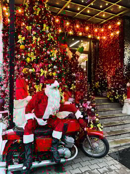 Santa Claus on a motorcycle beside festive Christmas tree decorations outside a shop photo