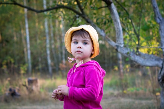 Little girl or child with sad expression wearing panama or hat on walk in park or village. Blurred background with trees or forest. Child portrait photo